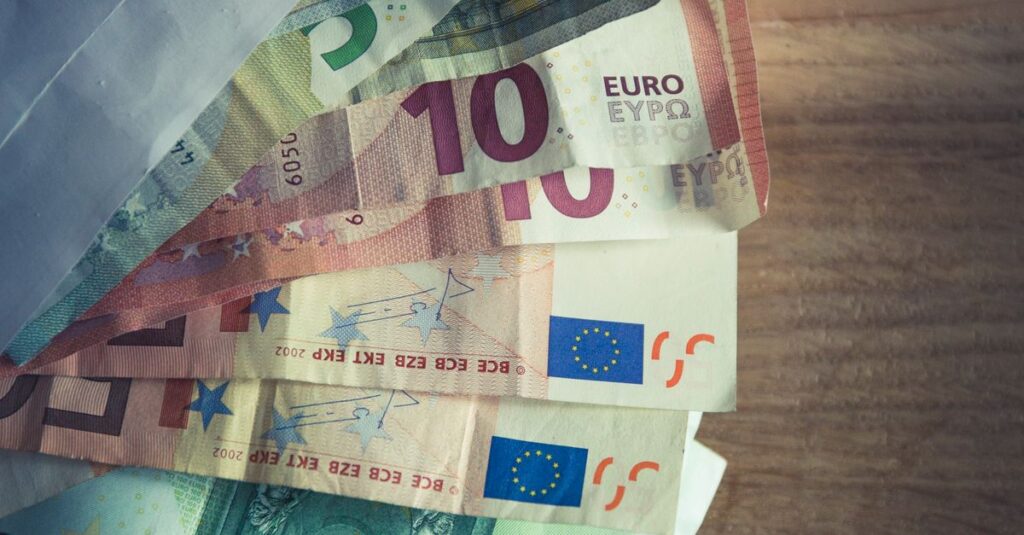 Trade finance meaning A collection of Euro banknotes emerging from an envelope on a wooden surface.