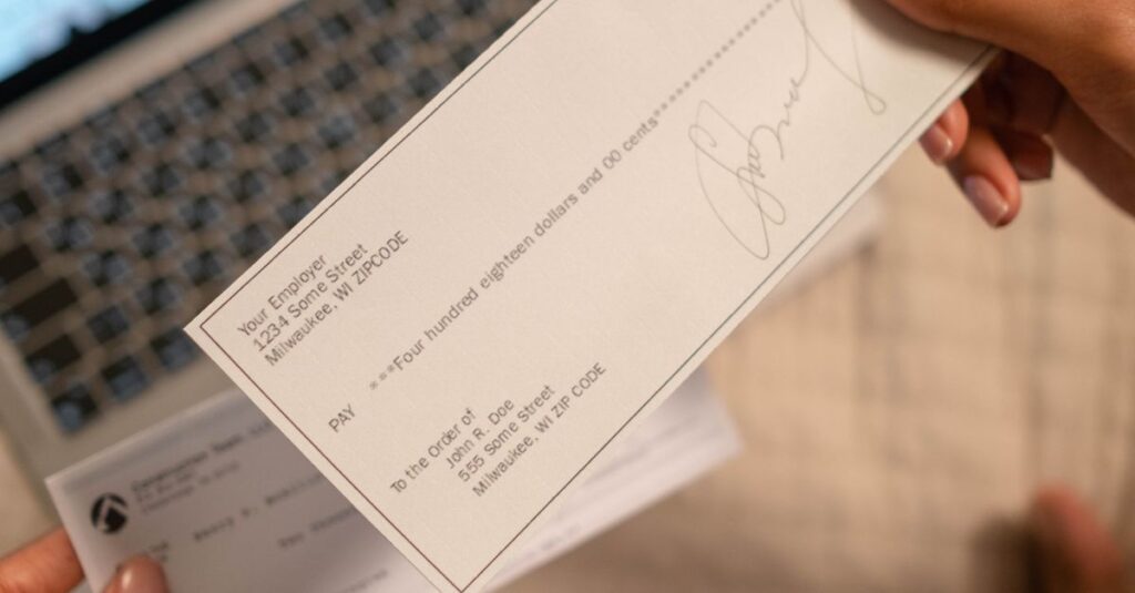 What is IEPF? Individual holding a cheque over laptop, signifying online banking or financial transaction.